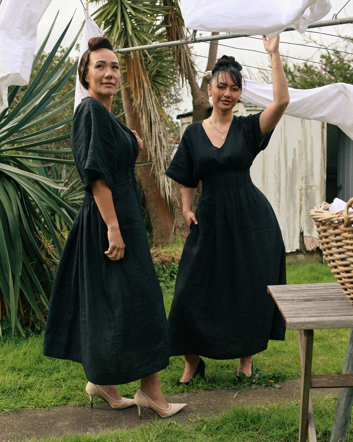 Two women at the clothesline wearing the Winnie black linen maxi dress