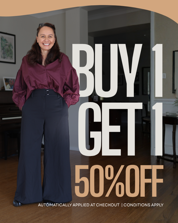 A woman stands in a living room wearing a burgundy long-sleeve button-up shirt and dark wide-leg pants, with large promotional text reading 'BUY 1 GET 1 50% OFF' overlaid on the right side.
